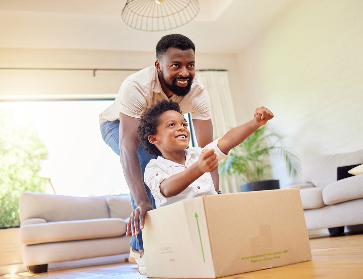 Father, son and playing at home with pretend car in a box on moving day in new property